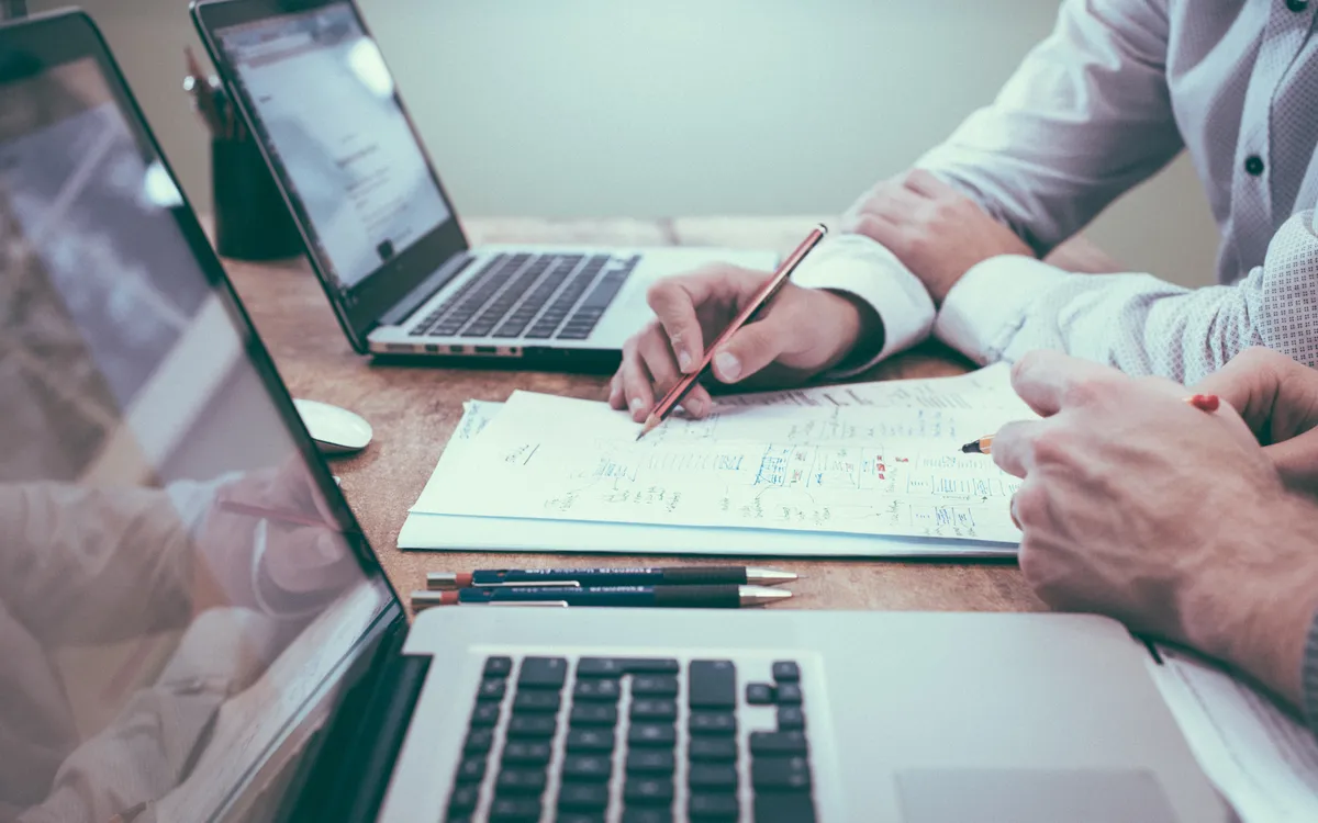 Twee mensen bespreken aantekeningen op papier naast hun laptops